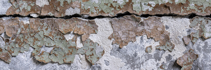 Peeling paint on the wall. Panorama of a concrete wall with old cracked flaking paint. Weathered rough painted surface with patterns of cracks and peeling. Wide panoramic texture for grunge background