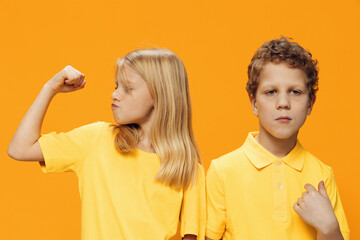 funny, funny school-age children stand on a yellow background in yellow clothes and show muscles to each other