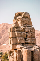 Ancient Egyptian Colossi of Memnon stone pharaoh statue with mountain background at Valley of the Kings in Luxor