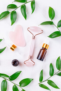 Rose quartz crystal facial roller and massage tool Gua sha with brown cosmetic bottles and leaves