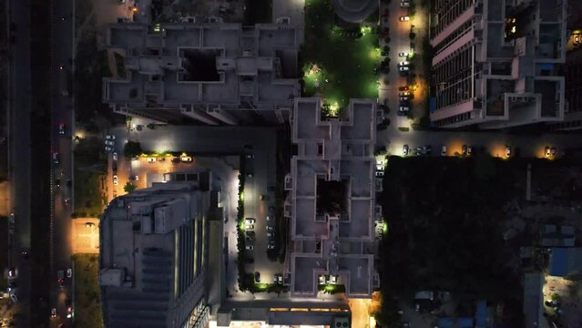 top down shot showing vehicles moving around around skyscrapers with parks with pools of light at dusk in gurgaon India