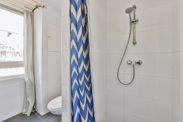 Shower faucets attached to tiled wall near glass partition and toilet ornamental curtail in...