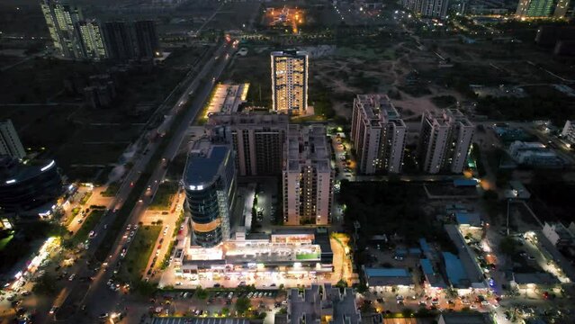 aerial drone night shot showing the bright lights and illuminated buildings, skyscrapers with homes offices and real estate with traffic moving around it in metro cities of India like delhi, mumbai