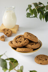 Chocolate chip cookies in a round platter with a jug of milk in the background.