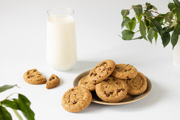 Chocolate chip cookies on a round plate, next to a glass of milk.