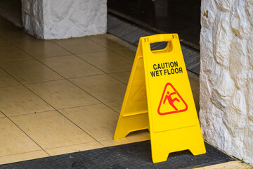 Wet floor caution sign on walkway near the building after raining. Warning yellow plastic caution wet floor sign on the ground with copy space.