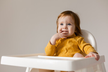 funny red-haired blue-eyed baby in a yellow bodysuit sitting in a white high chair