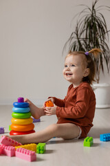 cheerful baby plays with a multi-colored pyramid and other educational toys sitting on the floor