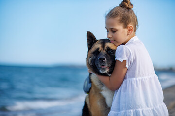 Teenage girl in light clothes hugs and loves dog friend of Akita Inu breed on beach near Black Sea...