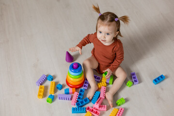 Fototapeta na wymiar cheerful baby plays with a multi-colored pyramid and other educational toys sitting on the floor