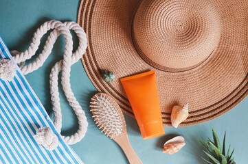 Flat lay summer travel photography. Striped bag, straw hat, orange sunscreen tube, wooden hair brush and seashells. Beach essentials, vacation packing