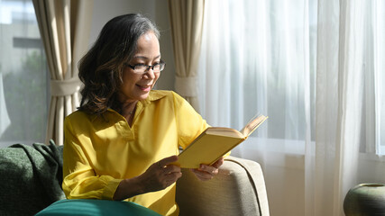 Relaxed middle age lady enjoying being at home and reading a book at home. Mature, leisure concept 