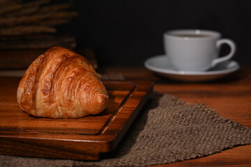 Fresh homemade butter croissant and coffee cup on wooden table. Breakfast, bread bakery products cafe concept