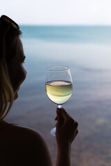 Girl looks at the sunset. A girl is holding a glass of wine. Sea. The sun. Backlight