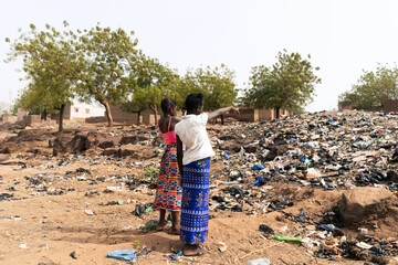 Two African girls pointing to the mountain of garbage that occupies the street of rural village...