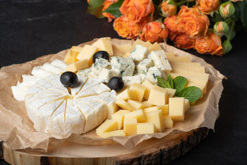 Cheese assortment on  plate with red roses on  a dark background.