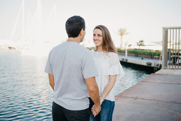 A stylish young man is holding hands with his brunette girlfriend in the port