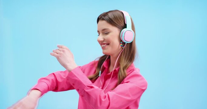 Close Up Portrait Of Joyful Caucasian Young Woman Dancing Having Fun Listening To Music In Colorful Headphones And Smiling. Beautiful Happy Female Model Dances On Blue Background, Positive Emotions