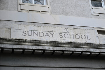 Sunday School sign, surrounded by cracks, engraved in the worn white wall of an old building