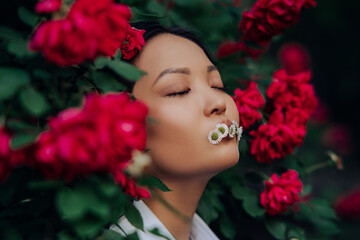 Portrait of young woman with chamomile flowers in her mouth among red rose.
