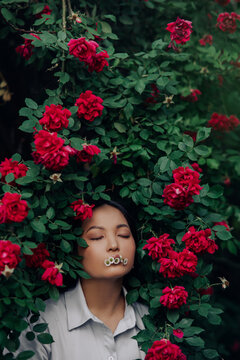 Portrait of young woman with chamomile flowers in her mouth among red rose.