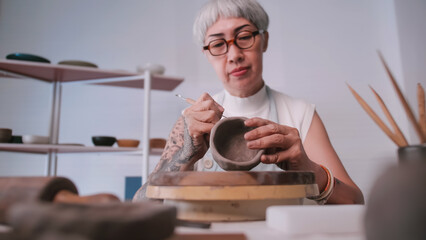 Asian elderly woman enjoying pottery work at home. A female ceramicist is making new pottery in a studio.