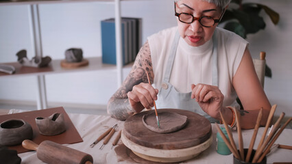 Asian elderly woman enjoying pottery work at home. A female ceramicist is making new pottery in a studio.