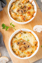 Baked julienne with mushrooms and chicken in a creamy sauce with cheese on top on a gray concrete background. Selective focus. Copy space.