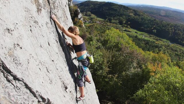 The girl climbs the rock, The climber trains on natural terrain,  A woman overcomes a difficult climbing route against the background of a blue sky