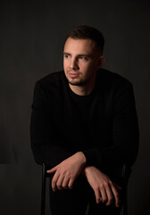 Obraz premium portrait of handsome man sitting on chair in dark studio 
