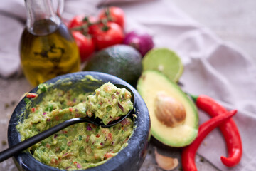 freshly made guacamole in marble mortar with ingredients on grey concrete background