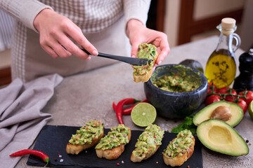 woman making bruschetta with freshly made guacamole on domestic kitchen