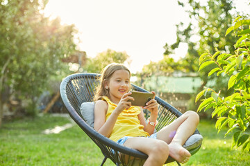 Happy kid girl playing game on mobile phone in the park outdoor