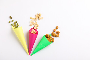 Indian snack, dry spicy nuts in paper cone on white background.