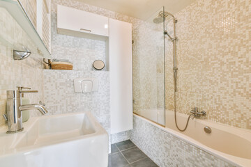 Bathtub with shower and glass partition placed in corner against sink and mirror in small light bathroom with beige tile walls