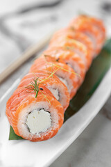 set of rolls philadelphia kappa with microgreens and green bamboo leaf in a white ceramic plate with chopstick on a bright textured marble background, side view, close-up