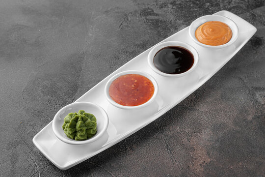 set of sauces for sushi on a white plate, wasabi, spicy, cheesy, soy. dark gray textured background, side view