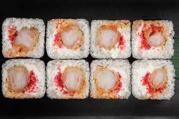 set of square maki rolls with tiger shrim, caviar and green bamboo leaf in a black ceramic plate with chopstick on a dark gray textured background, top view, close-up