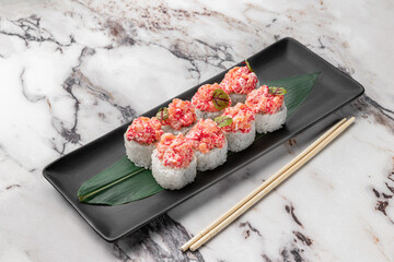 set of rolls with salmon, red flying fish caviar and green bamboo leaf in a black ceramic plate with chopstick on a bright textured marble background, side view