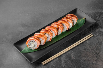 set of maki rolls with smoked eel and green bamboo leaf in a black ceramic plate with chopstick on a dark gray textured background, side view