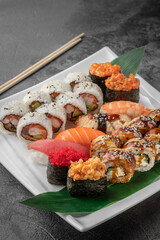 set of different colorful maki sushi rolls, nigiri and gunkan with tiger shrimp, tomago, salmon, tuna, chuka salad, flying fish caviar, tuna and green bamboo leaf in a white ceramic plate, close-up