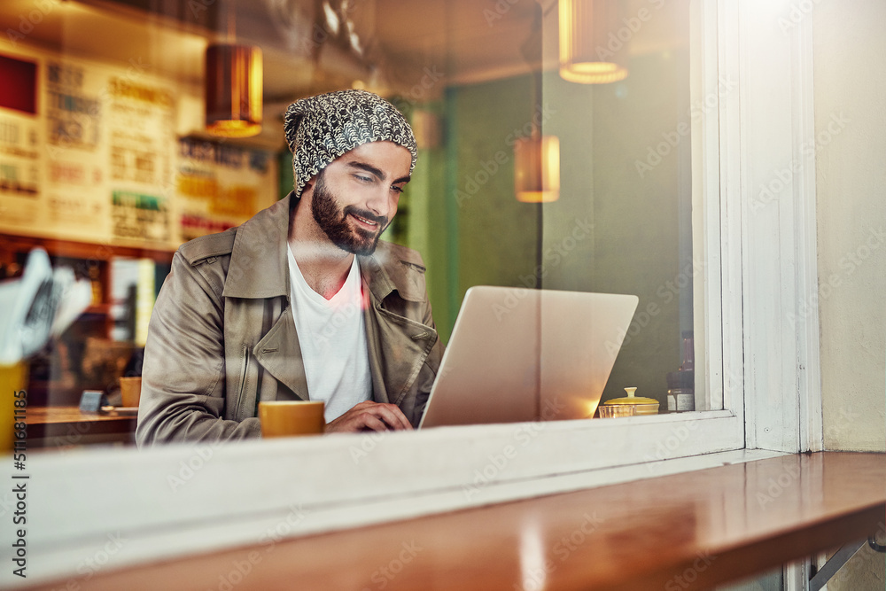 Poster Getting online at his local cafe. Shot of a handsome young man sitting at a cafe counter using a laptop.