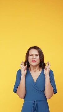 Make a wish. Good luck. Dream hope expectation. Worried excited woman in blue begging with crossed fingers isolated on bright orange vertical empty space background.
