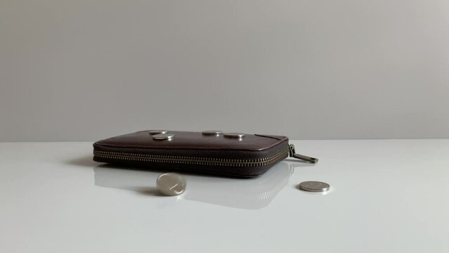 Coin Rotating And Spinning On Desk. Dark Burgundy Wallet With Silver Coins On A Gray Background.