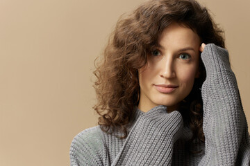 Close up portrait of cute curly beautiful female in gray warm casual sweater hold hands near face...