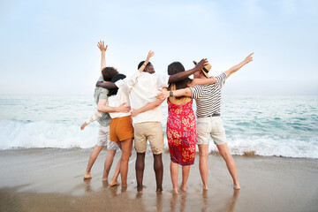 A group of friends with their backs to the camera enjoying the sea together - Multicultural...