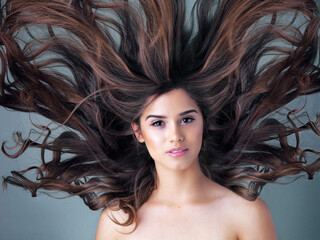 Big hair, big dreams. Studio shot of a beautiful young woman posing against a gray background.