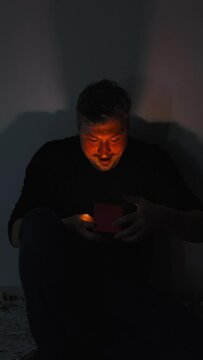 Christmas surprise. Curious man. Festive gift. Holiday miracle. Amazed shocked guy opening present box neon light red glow shining dark shadow interior vertical.