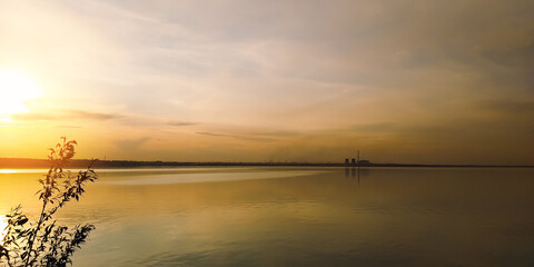 The sun at sunset over a branch of a large lake and factories on the horizon