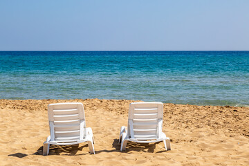 Sunloungers on a sandy beach with a view out to sea, at Golden Beach in Cyprus